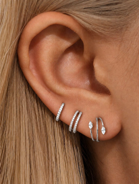 Three silver CZ hoops styled on multiple lobe piercings, featuring single pavé, double-row and marquise spiral designs.