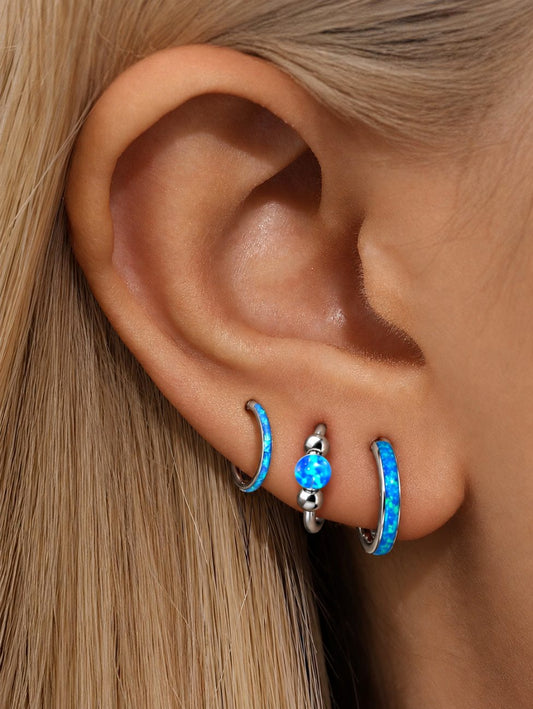 Close-up ear styling with three silver G23 titanium blue opal hoops, featuring a slim opal clicker, blue opal bead hoop and wide opal hoop.