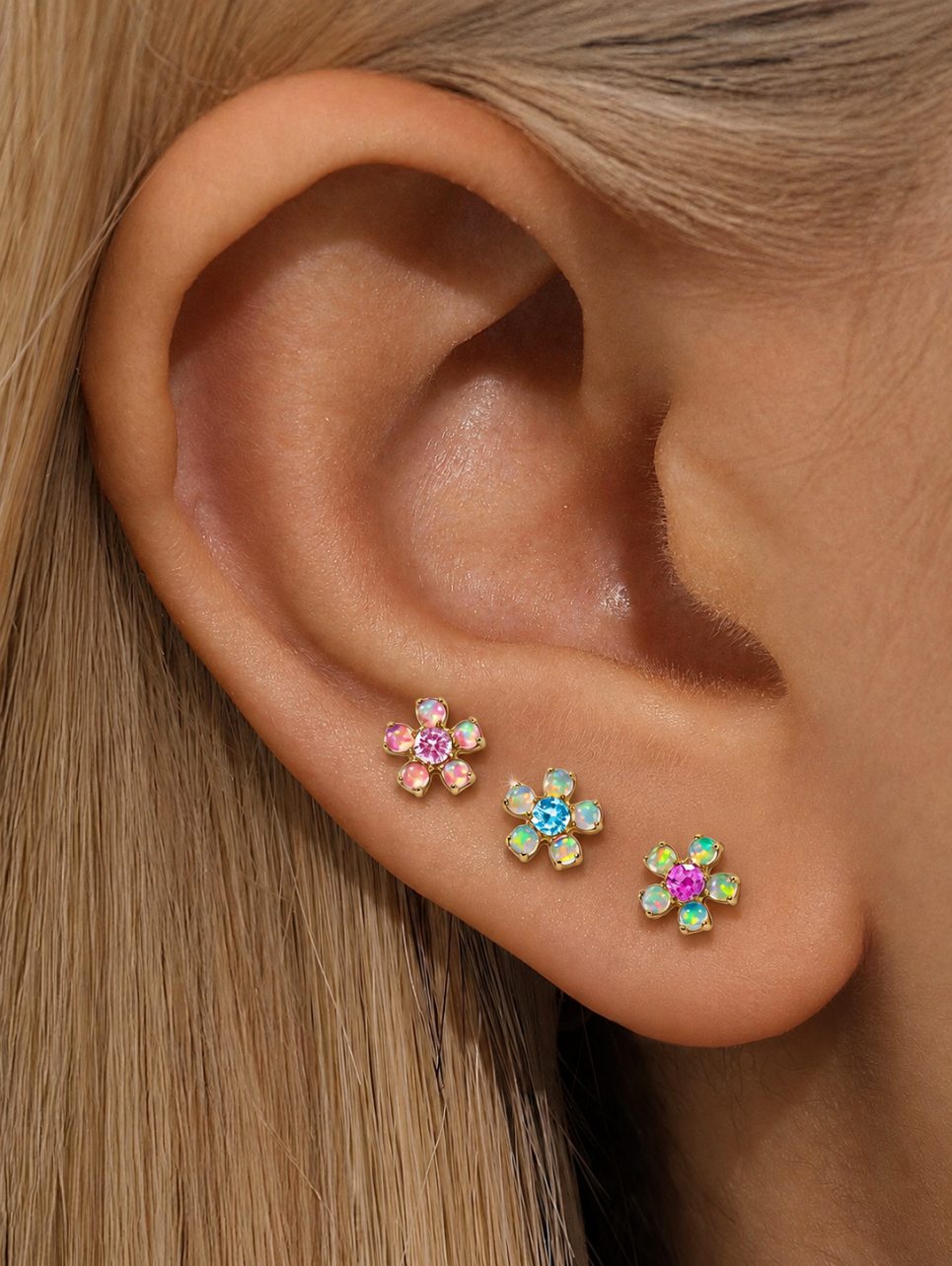 Three G23 titanium rainbow opal flower flat back earrings styled on the ear in pink, aqua blue and hot pink
