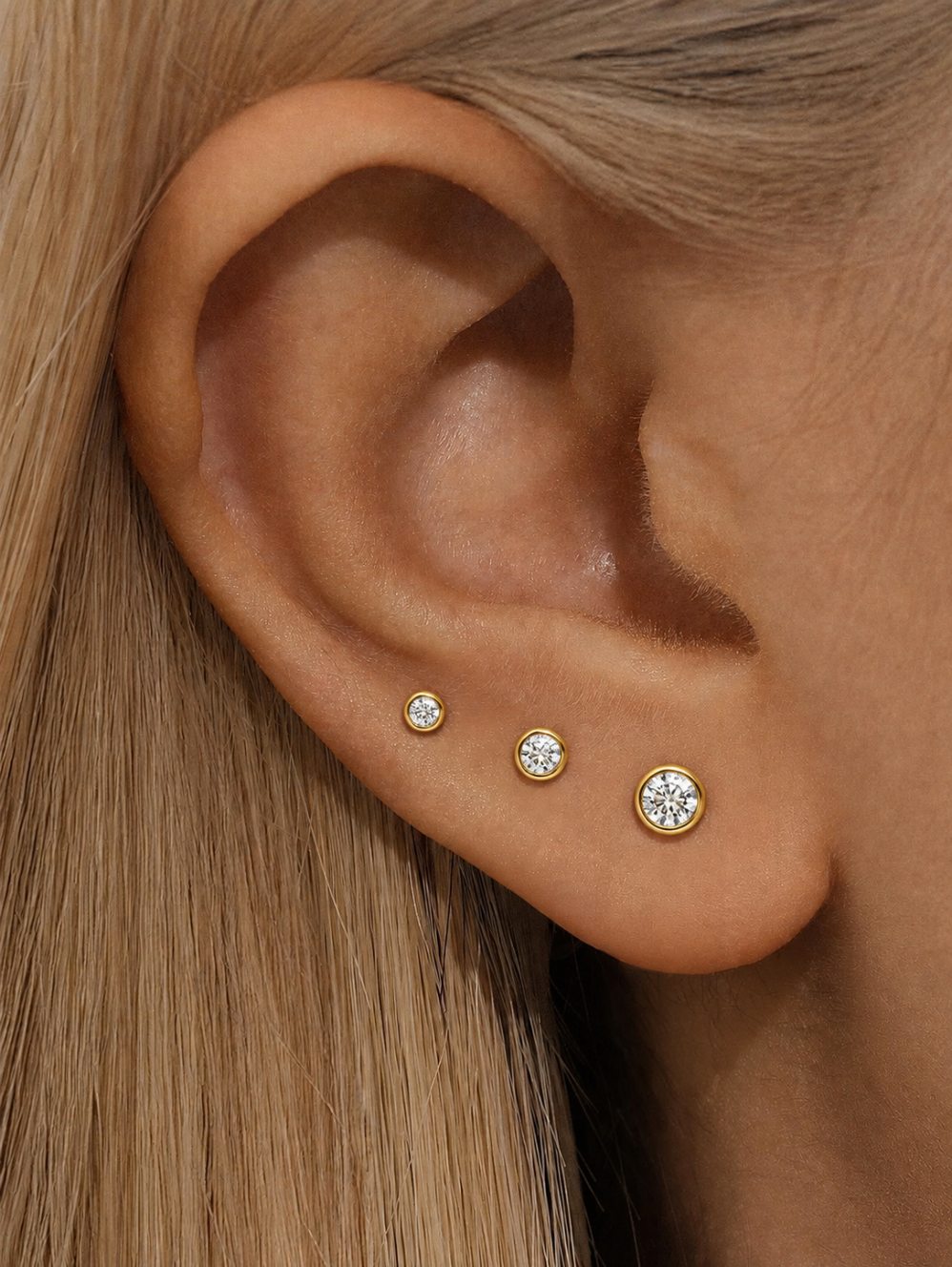 Gold moissanite sterling silver flat back studs in three sizes worn on the lobe