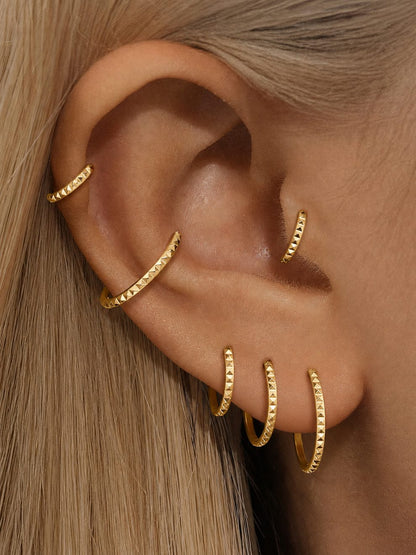 Gold pyramid-faceted clicker rings styled in a curated ear stack