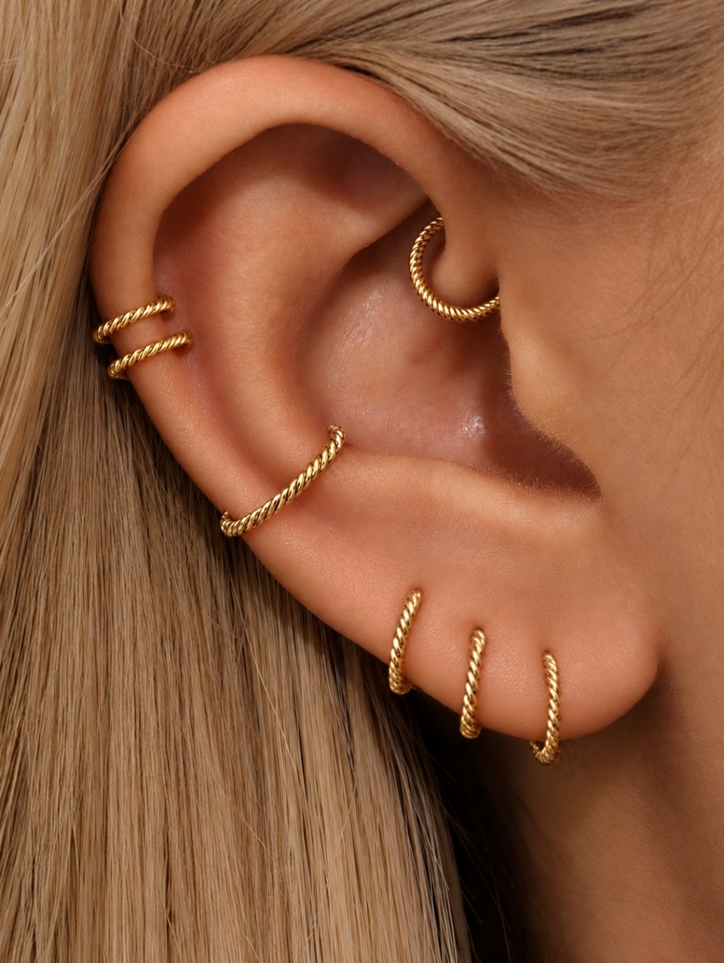 Gold twisted G23 titanium clicker hoops styled across lobe, helix and inner ear piercings