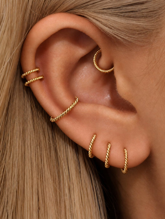 Gold twisted G23 titanium clicker hoops styled across lobe, helix and inner ear piercings