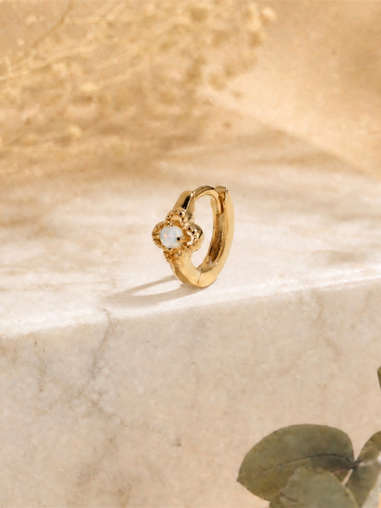 Gold opal flower clicker hoop earring displayed on marble surface