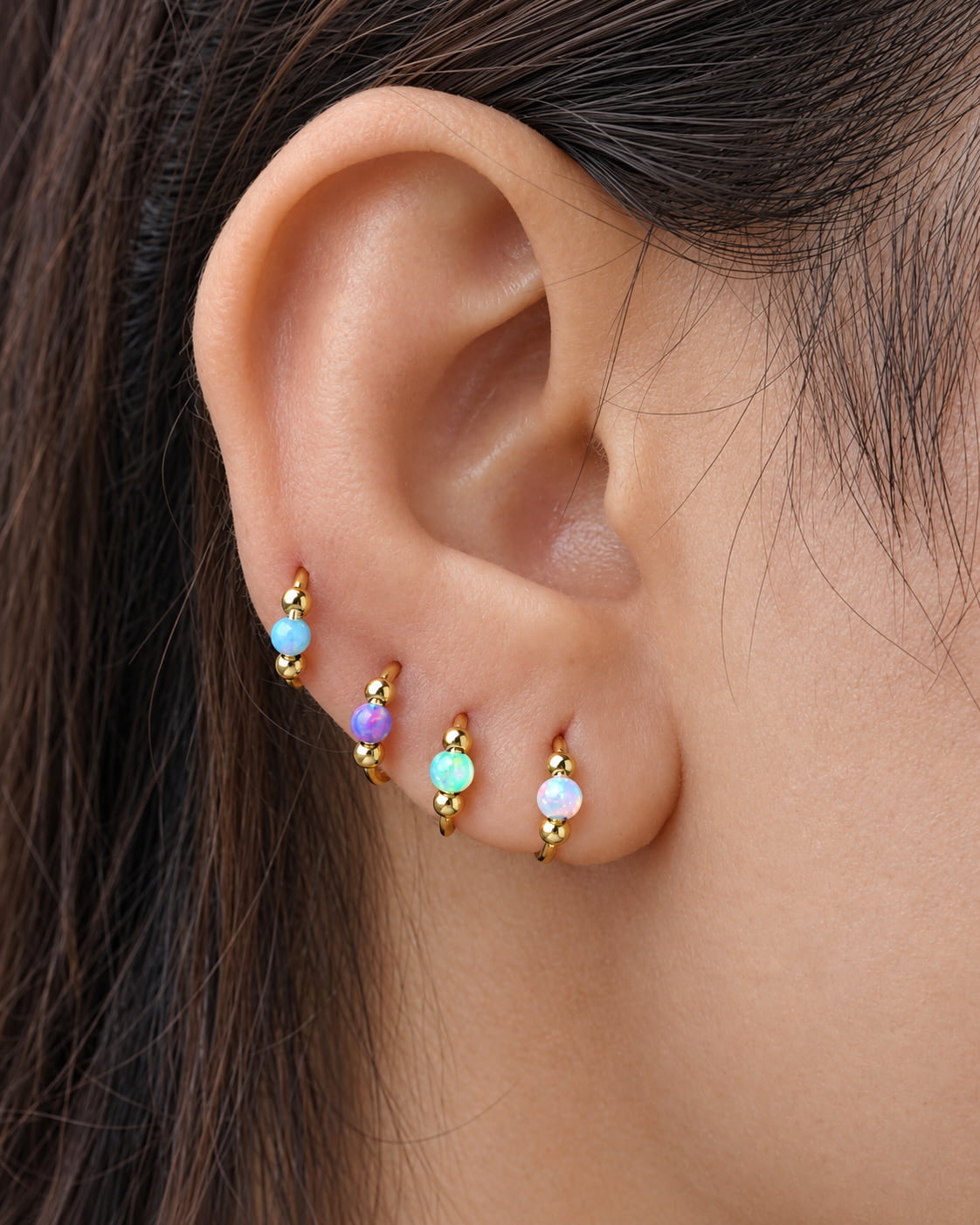 G23 titanium opal clicker rings worn on multiple ear piercings in light blue, purple, green and white opal