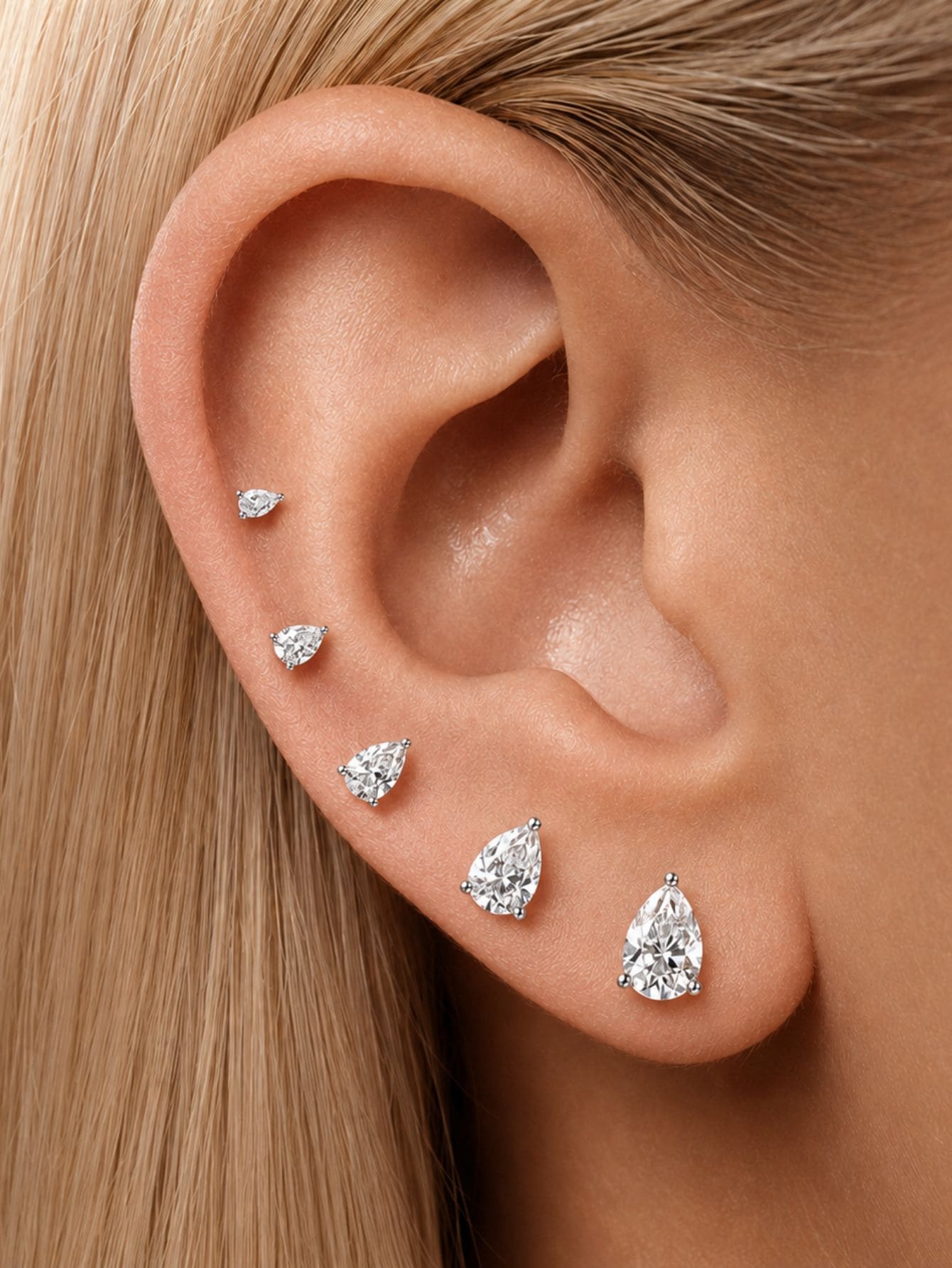 Pear-cut moissanite flat back studs styled in graduated sizes on the ear