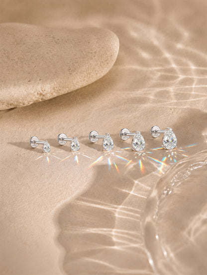 Pear-cut moissanite flat back studs in five sizes on a warm neutral background